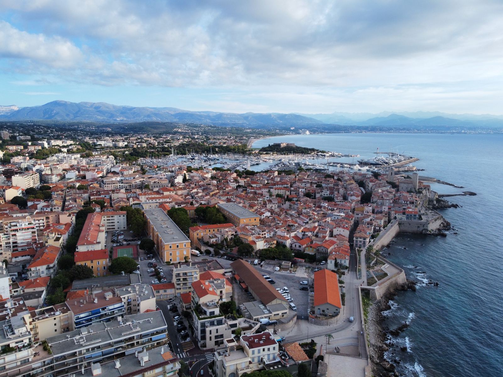 Antibes old town from above — the walled city on a headland, terracotta rooftops, mountains, Mediterranean all around